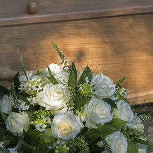 Bouquet of white roses next to a coffin.